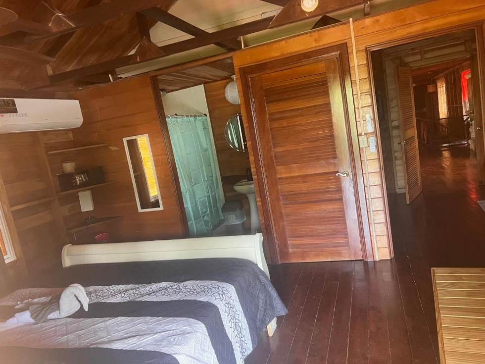 A bedroom in the Deluxe Family Suite: a bed with a grey quilt, air conditioning, open shelving and a private shower room through the doorway.
