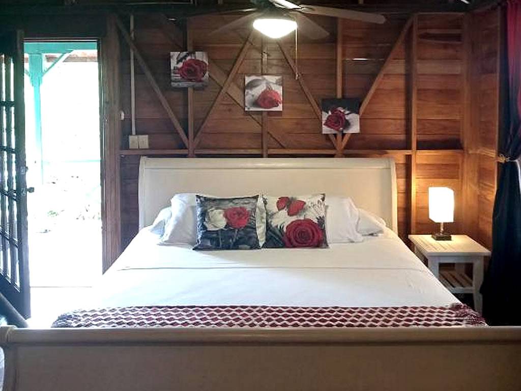 The sleigh bed made up in white, framed by timber walls, with a lamp on the bedside table and the doors open to one side.