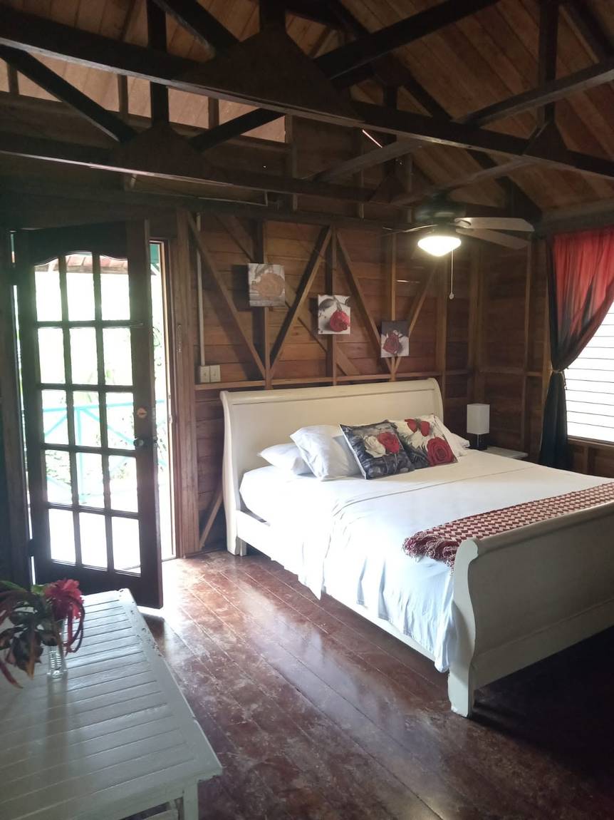 A bedroom in the suite: a white sleigh bed under an open beamed roof, with french doors standing open onto the deck and a ceiling fan above.