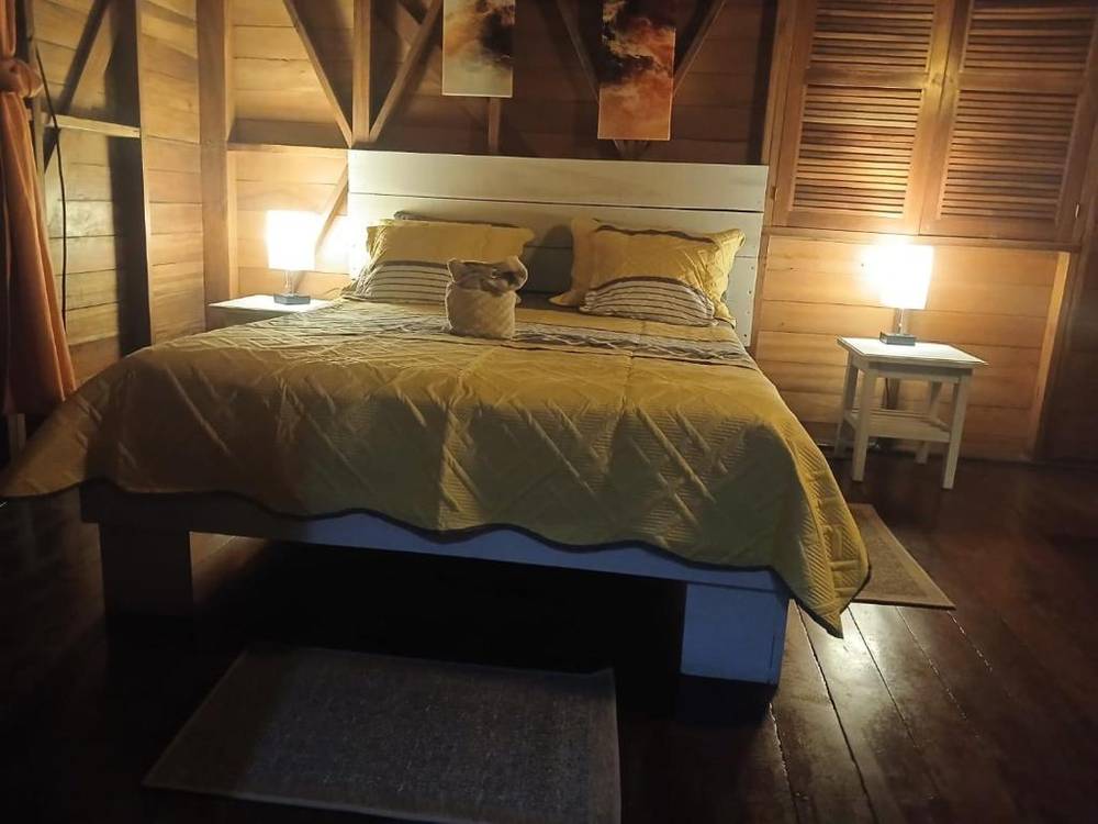 The Superior Double: a double bed with a yellow quilt between two lamps, under a hardwood ceiling, with louvred doors to one side.